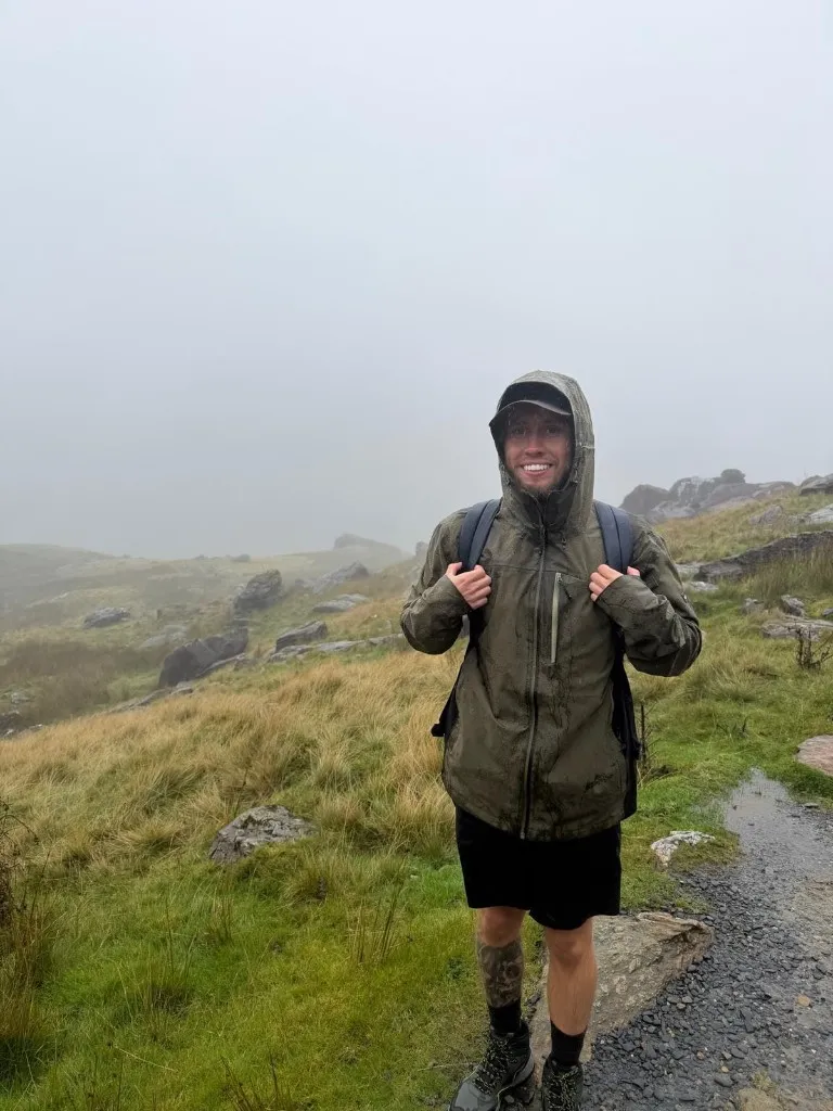A smiling challenge participant standing on a wet mountain trail
