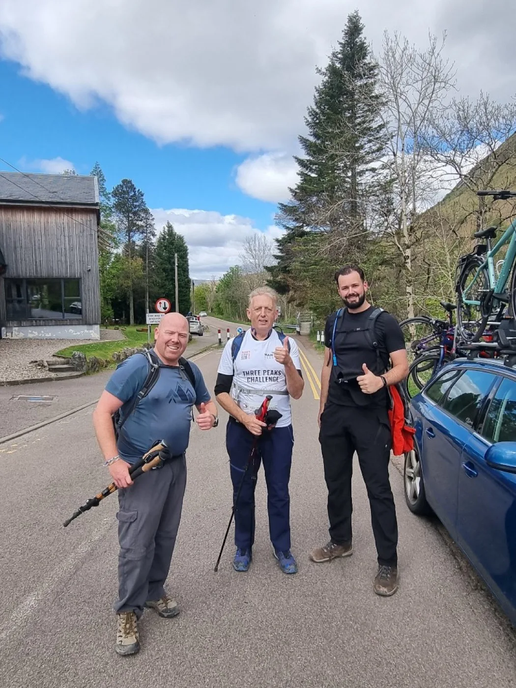 Three climbers ready for the next peak, standing roadside with hiking poles and backpacks