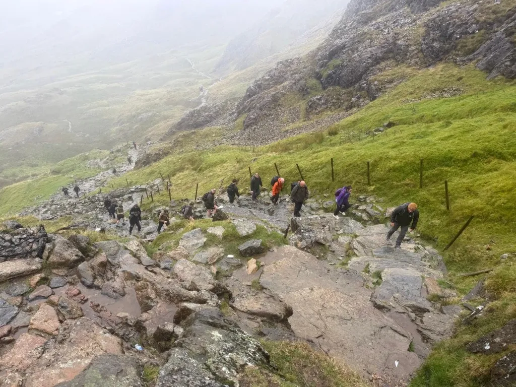 Three Peaks participants climbing a steep rocky mountain path in the rain