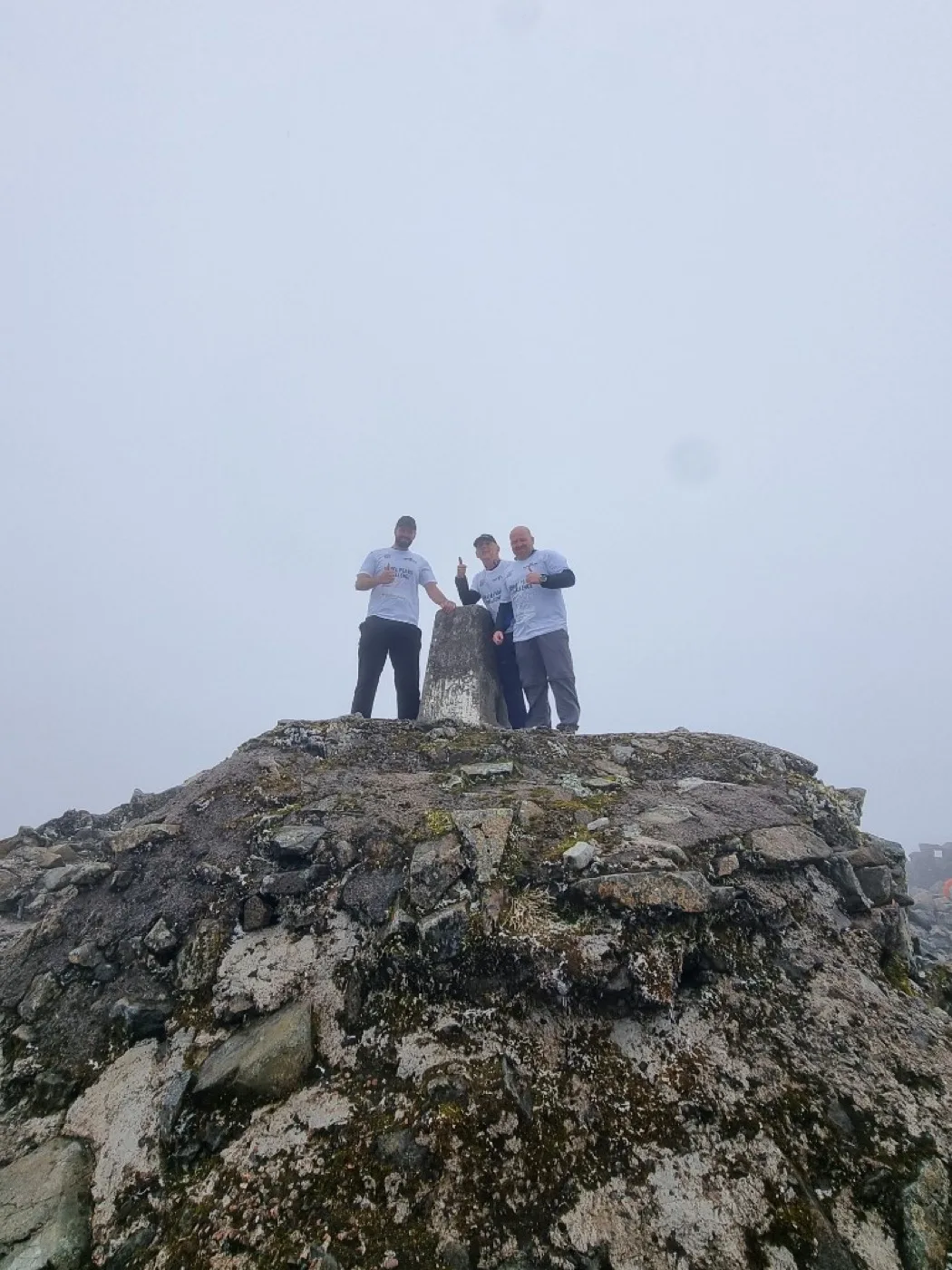 Three climbers at a misty mountain trig point during the Three Peaks Challenge