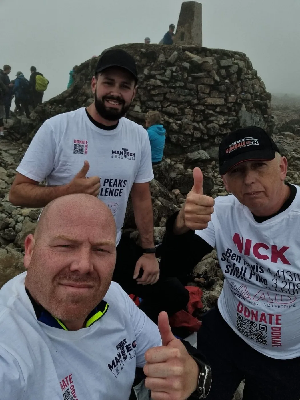 Mantech team selfie at a rocky summit, wearing donate QR code Three Peaks Challenge shirts