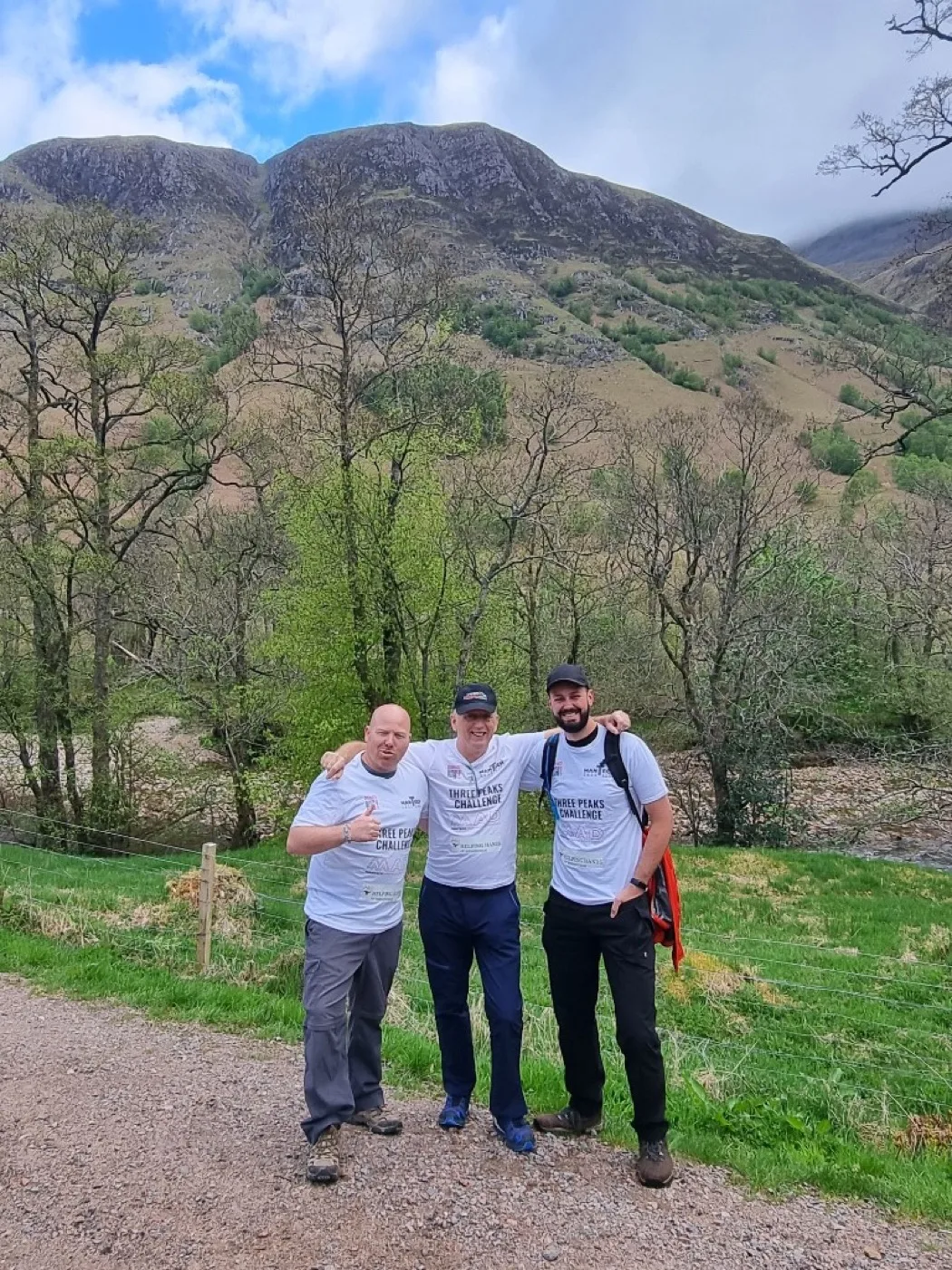 Three Mantech teammates with arms around each other on a mountain path, Three Peaks Challenge shirts visible