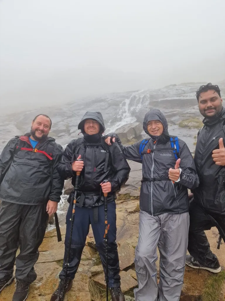 Four members of the Three Peaks team standing together beside a mountain waterfall