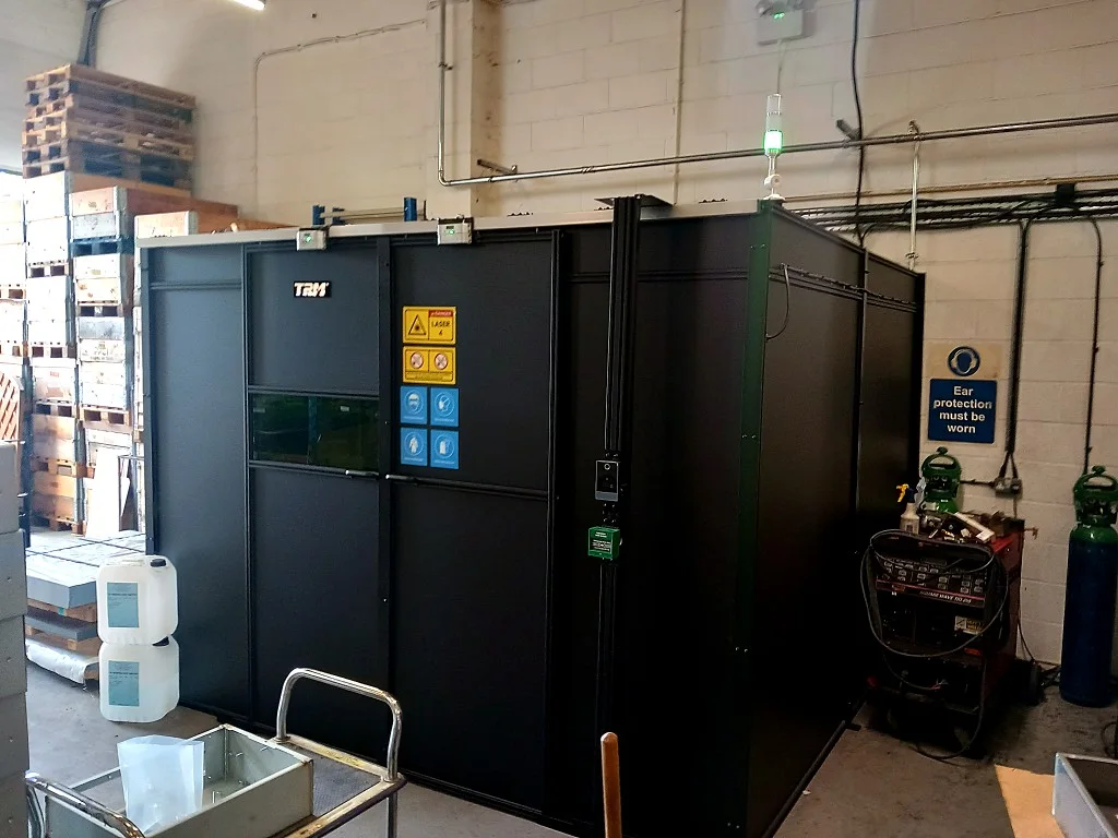 TRM laser welding enclosure with viewing window and Class 4 safety signage, installed in a Wokingham fabrication workshop
